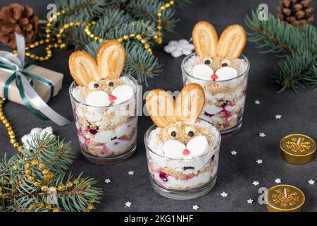 Kuchen ohne Backen in Form von niedlichen Kaninchen in Gläsern mit Kirschen, Keksen und Quark-Creme auf grauem Hintergrund. Symbol des neuen Jahres 2023 Stockfoto