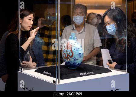 Hongkong, China: 21. November 2022. Bonhams Chinesische Keramik und Verkauf von Kunstwerken Gigi Yu (L), Bonhams Head of Chinese Ceramics and Works of Art, zeigt die Liddell Moonflask. Einer von nur drei bekannten, noch erhaltenen türkisfarbenen Unterglasur-blauen und kupferroten ‘Dragon' Qianlong (vierter Qing-Kaiser, der von 1735 bis 1796 über China regierte) Mondkolben tritt nach einem Jahrzehnt auf den Markt. Die außergewöhnlich seltene Liddell Moonflask aus der angesehenen Huaihaitang Collection（懷海堂）aus Hongkong trägt eine Schätzung von 18.000.000 HK-25.000.000 Alamy Live News/Jayne Russell Stockfoto