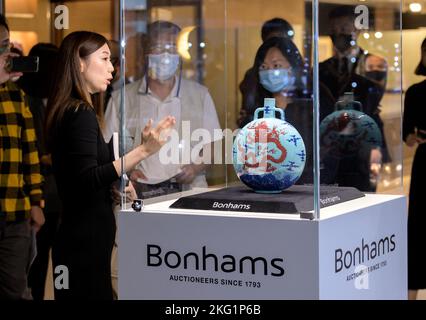 Hongkong, China: 21. November 2022. Bonhams Chinesische Keramik und Verkauf von Kunstwerken Gigi Yu (L), Bonhams Head of Chinese Ceramics and Works of Art, zeigt die Liddell Moonflask. Einer von nur drei bekannten, noch erhaltenen türkisfarbenen Unterglasur-blauen und kupferroten ‘Dragon' Qianlong (vierter Qing-Kaiser, der von 1735 bis 1796 über China regierte) Mondkolben tritt nach einem Jahrzehnt auf den Markt. Die außergewöhnlich seltene Liddell Moonflask aus der angesehenen Huaihaitang Collection（懷海堂）aus Hongkong trägt eine Schätzung von 18.000.000 HK-25.000.000 Alamy Live News/Jayne Russell Stockfoto