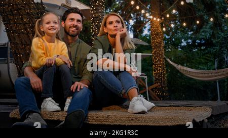 Kaukasische Familie sitzt in der Nähe von Camp in Camping in der Nähe von van Anhänger Blick auf den Himmel auf der Natur erzählt Geschichten sprechen Kind Tochter Mutter und Vater reden Stockfoto