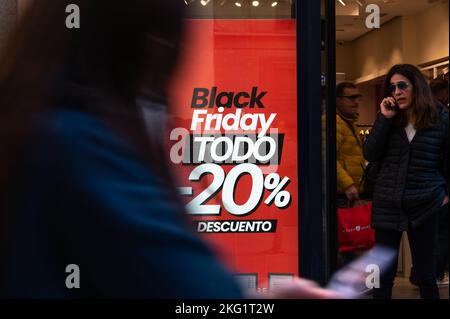 Die Leute gehen vorbei an einem Schild, auf dem ein Preisnachlass für Black Friday am Schaufenster eines Ladens in der Innenstadt von Madrid angekündigt wird. Stockfoto