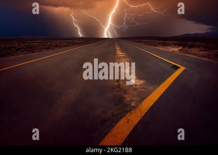 Eine Aufnahme einer Wüstenstraße mit einem intensiven Gewitter und Blitzen am Himmel aus tiefem Winkel Stockfoto