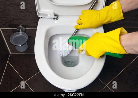 Reiniger in gelben Gummihandschuhen reinigt die Toilettenschüssel mit einer Bürste und einem Desinfektionsmittel Stockfoto