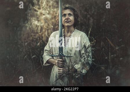 Schöne Frau in der Natur mit einem Schwert in der Hand. Stockfoto