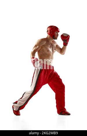 Junge professionelle Kickboxer trägt Helm und Boxhandschuhe in Bewegung isoliert auf weißem Hintergrund. Sport, Wettkampf, Energie, Kampfsport Stockfoto