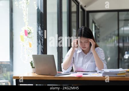 Müde asiatische Geschäftsfrau mit Kopfschmerzen im Büro, krank, gestresst bei der Arbeit Stockfoto