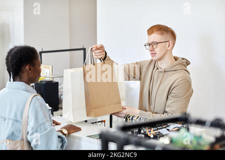 Porträt eines männlichen Ladenmanagers, der Papiertüten mit Einkäufen über den Ladentisch an den Kunden übergab Stockfoto