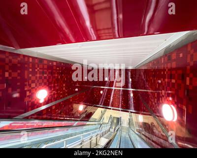 In einer U-Bahn-Station. Eine lange Rolltreppe bewegt sich tief nach unten in roter Farbe in der Innenausstattung der Wände. Transit zu einer anderen Position. Singapur. Stockfoto