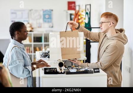 Seitenansicht Porträt eines männlichen Geschäftsleiters, der dem Kunden Papiertüten mit Einkäufen über den Ladentisch überreicht Stockfoto