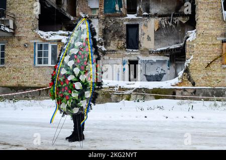 Non Exclusive: HORENKA, UKRAINE - 19. NOVEMBER 2022 - Ein Mann hält einen Trauerkranz vor einem fünfstöckigen Wohngebäude, das von einer russischen aer zerstört wurde Stockfoto