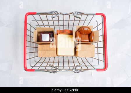 Auswahl an wichtigen Möbelfiguren und winzigen Lieferkartons in einem Einkaufswagen, Draufsicht. Neues Einrichtungskonzept für Apartments. Stockfoto