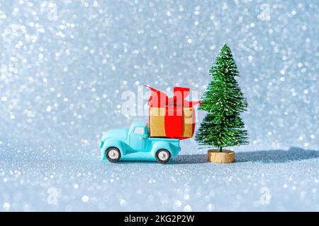 Ein kleiner blauer Bauernhof-Pickup liefert ein Weihnachtsgeschenk unter einem Spielzeugbaum. Weihnachtsdekoration Konzept. Stockfoto