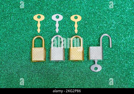 Reihe mit vier glänzenden Metallvorhängeschlössern und Hauptschlüsseln, isoliert auf grün glänzendem Hintergrund. Creative Banking Secrecy Concept. Stockfoto