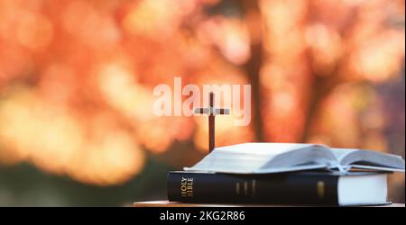 Rote Ahornblätter und Herbstbäume im Wald und das Heilige Kreuz Jesu Christi und bibelbuch auf dem Tisch Stockfoto