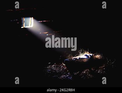 Helles Licht aus dem Fenster beleuchtet das Jesuskind in der Krippe, Weihnachten und Weihnachten im Hintergrund, um die Geburt Jesu Christi zu feiern Stockfoto