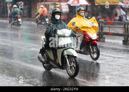 Vietnamesen mit Helm und Regenmantel fahren bei starkem Regen Motorrad, Wasser auf der Straße. Regenzeit in Saigon, Ho-Chi-Minh-Stadt. Vietnam. Stockfoto