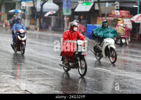 Vietnamesen mit Helm und Regenmantel fahren bei starkem Regen Motorrad, Wasser auf der Straße. Regenzeit in Saigon, Ho-Chi-Minh-Stadt. Vietnam. Stockfoto
