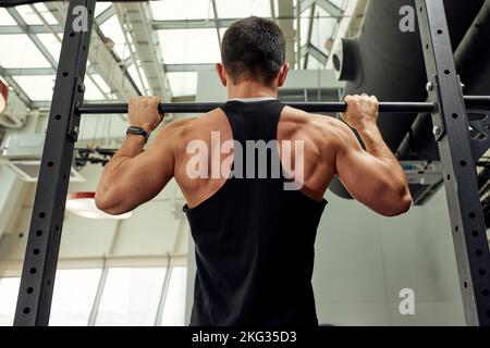 Arbeiten Sie mit eigenem Gewicht, der Athlet macht Übungen auf den unebenen Balken Stockfoto