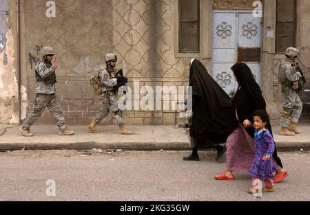 MOSUL, IRAK - 12. April 2006 - Soldaten der US-Armee winken und lächeln, als sie bei einer Fußstreife in Mosul an zwei irakischen Frauen und einem Kind vorbeikommen. Stockfoto