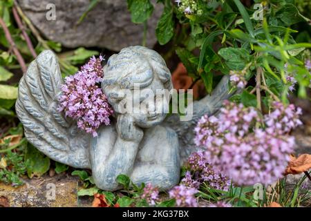 Kleine Engelsfigur im Garten zwischen Blumen Stockfoto