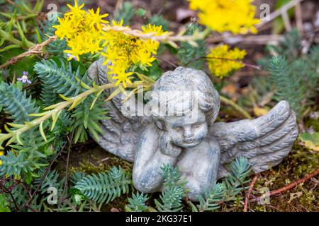 Kleine Engelsfigur im Garten zwischen Blumen Stockfoto