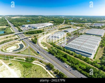 Drohnenaufnahme der entwickelten Autobahn-Doppelbrücke, umgeben von Gewerbegebiet und üppigem Grün Stockfoto