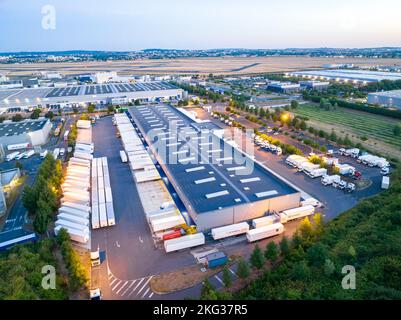 Blick aus der Vogelperspektive auf die Lagergebäude mit Lastwagen, die in der Laderampe geparkt sind und von üppigem Grün umgeben sind Stockfoto