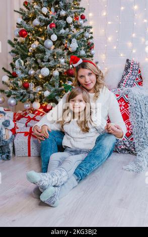 Glückliche Mutter und Tochter sitzen zwischen Geschenkschachteln auf dem Hintergrund des Weihnachtsbaums Stockfoto