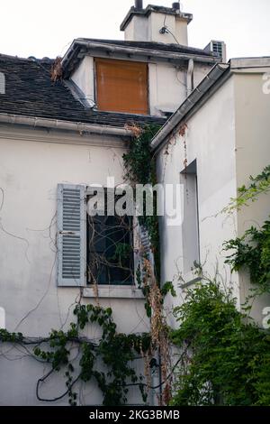 Ein altes traditionelles Haus mit grünen Pflanzen, das in der Nähe der hölzernen Fensterläden in Paris, Frankreich, klettert Stockfoto