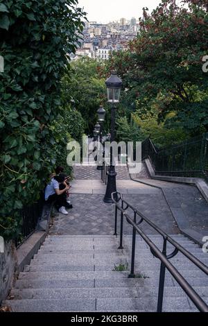 Eine vertikale Aufnahme von zwei Personen, die auf der Treppe zur Basilika des Heiligen Herzens von Paris, Frankreich, sitzen Stockfoto