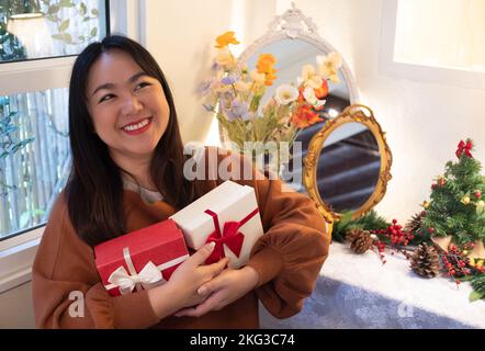 Glückliche asiatische Frauen lächeln und Geschenkboxen halten, mit Weihnachtsdekoration im Hintergrund Stockfoto