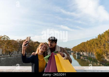 Ein Paar aus mehreren Rassen, das ein sehr glückliches Selfie mit Einkaufstaschen macht Stockfoto