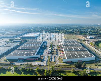 Luftaufnahme von zwei großen Lagerhausgebäuden in der Nähe der Autobahn über neu entwickelte gewerbliche Immobilieninfrastrukturen, umgeben von üppigem Grün Stockfoto