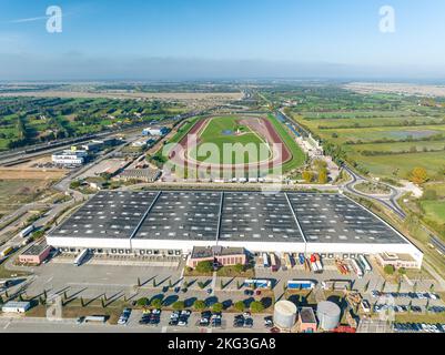 Luftaufnahme des Lagerhauses mit Lastwagen, die in der Laderampe geparkt sind, sowie Personalparkplatz, ovaler Sportplatz mit Grünflächen Stockfoto