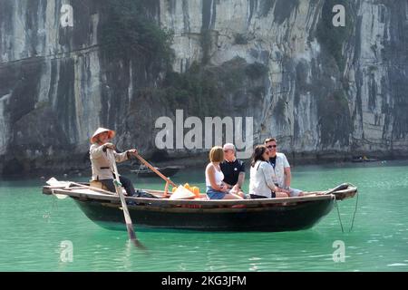 Touristen sehen die Sehenswürdigkeiten von einem traditionellen hölzernen Ruderboot mit freundlicher Genehmigung eines lokalen schwimmenden Dorfes in der Halong-Bucht, Vietnam Stockfoto