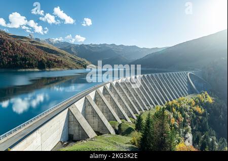 Aus der Vogelperspektive sehen Sie das Wasserkraftwerk am Roselend-See mit einer schmalen Straße auf einem Bögen-Damm aus Beton und einem Wasserreservoir in den französischen Alpen Stockfoto