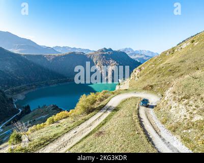 Atemberaubende Luftaufnahme von der Ecke des Berges, wo ein Auto von einer unbefestigten Straße in der Nähe des glitzernden Sees in Europa Frankreich vorbeifährt. Stockfoto