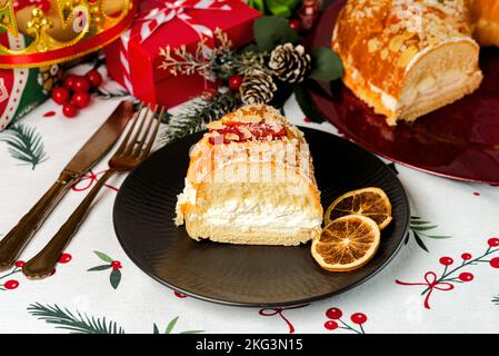 Eine Portion Roscon de reyes mit Sahne und weihnachtsschmuck auf einem schwarzen Teller über der weihnachts-Tischdecke. Kings Day Concept spanisch Three Kings Torte.T Stockfoto