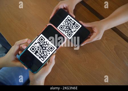 Frauenhand verwendet eine Mobiltelefonanwendung, um QR-Codes in Geschäften zu scannen, die digitale Zahlungen ohne Geld auf dem Tisch annehmen. QR-Code-Zahlung und c Stockfoto