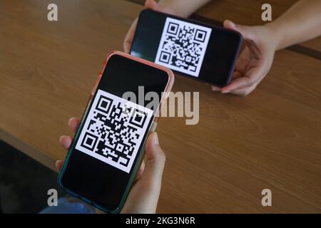 Frauenhand verwendet eine Mobiltelefonanwendung, um QR-Codes in Geschäften zu scannen, die digitale Zahlungen ohne Geld auf dem Tisch annehmen. QR-Code-Zahlung und c Stockfoto