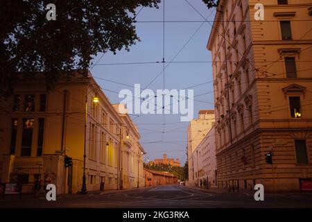 Leere Straße in Rom, Italien bei Sonnenuntergang. Postkarte der romantischen Ewigen Stadt zur goldenen Stunde. Gebäude in warmem Licht, Himmelblau, Drähte bilden ein Netz. Stockfoto