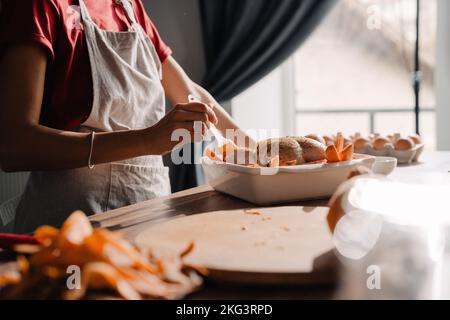 Junge Frau trägt Schürze Kochen Huhn in der Küche zu Hause Stockfoto