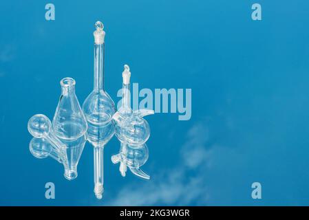 Verschiedene Laborglaswaren auf einem spiegelnden Hintergrund mit Himmelsreflexion. Konzeptionelle Labortests und Erforschung natürlicher Phänomene und Ressourcen Stockfoto