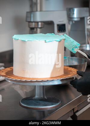 Kuchendesigner glättet einen mattierten, leeren Kuchen mit türkisblauer Buttercreme und Spachtel Stockfoto