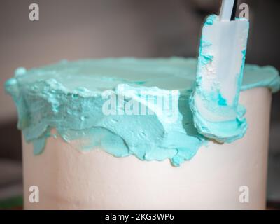 Kuchendesigner glättet einen mattierten, leeren Kuchen mit türkisblauer Buttercreme und Spachtel Stockfoto