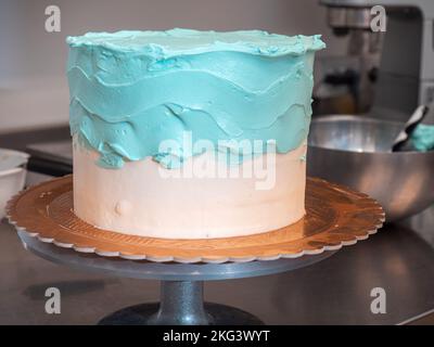 Kuchendesigner glättet einen mattierten, leeren Kuchen mit türkisblauer Buttercreme und Spachtel Stockfoto