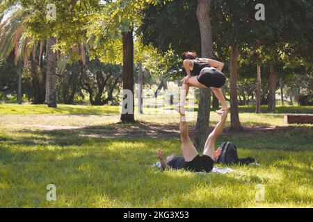 Valencia, Spanien - September 11 2022: Ein junges erwachsenes Paar in einem öffentlichen Park übt acroyoga, eine Form von Yoga Stockfoto