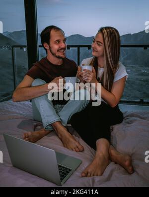 Nettes Paar in einem gemütlichen Zuhause, das auf dem Bett sitzt und Tee trinkt Stockfoto