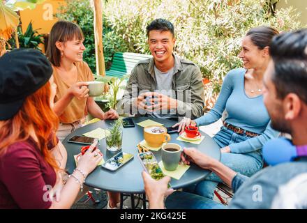 Von oben Gruppe von fröhlichen multirassischen Männern und Frauen, die über Witz lachen, während sie um den Tisch sitzen und frischen Kaffee am Sommerwochenende trinken Stockfoto