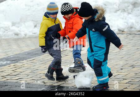 KIEW, UKRAINE - 19. NOVEMBER 2022 - drei Jungen treten einen Schneeball, Kiew, Hauptstadt der Ukraine. Stockfoto